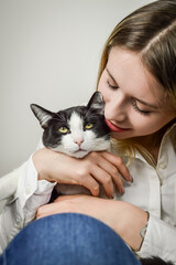 beautiful young blonde woman cuddling a bored looking young black and white cat close up