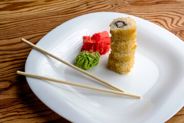 baked sushi stacked on top of each other with eel wasabi ginger and chopsticks on a white plate