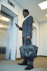 Vertical full length portrait of African-American businessman waiting for elevator in office...