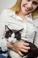 Portrait of a beautiful young blonde woman smiling while holding a black and white cat looking bored