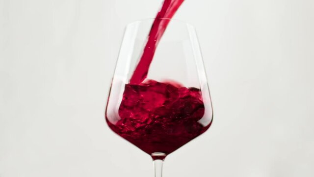 Red wine forms beautiful wave. Close-up shot. Wine pouring in wine glass over balack background. Slow motion of pouring red wine from bottle into goblet