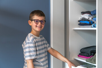 A little boy near the closet with clothes, chooses what to wear.