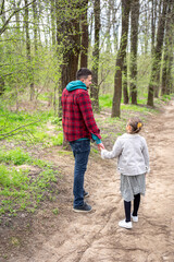 Little girl with dad is walking in the spring forest, holding hands.