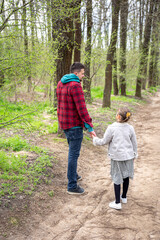 Fototapeta premium Little girl with dad is walking in the spring forest, holding hands.
