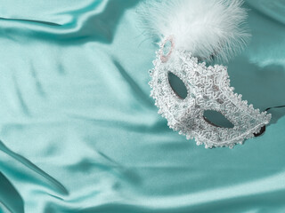 White venetian carnival mask with feather on green satin textile background