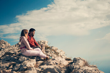 Fototapeta na wymiar Couple sits on a rock, looking at the landscape and enjoying the view and fresh air.