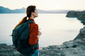 woman tourist at sunset near the sea in the mountains with a backpack on his back