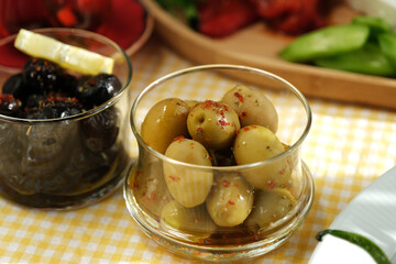 Green and black olives with chili peppers and thyme in a glass bowl.