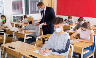 Teacher in protective mask explains to the students the subject of instruction in the classroom