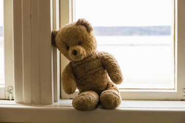 A lonely old teddy bear sits on the windowsill. Sadness, loneliness and isolation concept