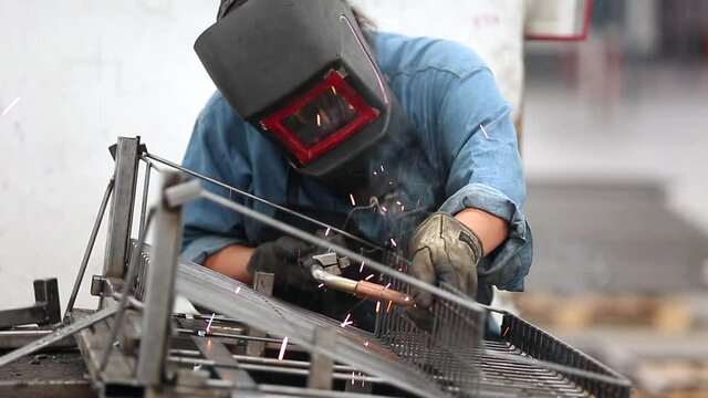 Mexican woman welding metal parts on factory