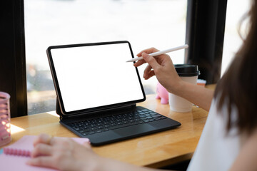 Mockup image of a woman hand using stylus with a black tablet with white blank screen on wooden desk.