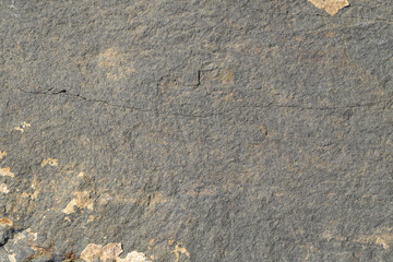 The texture of the surface of gray stone with cracks and light spots of layered rocks.
