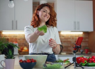 Young pretty woman blogger shoots a video of a salad recipe on a smartphone camera.