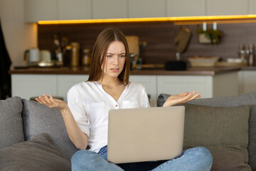 Dissatisfied caucasian young woman looking at laptop screen, reading bad news in message or having...