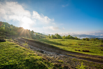 sunrise in summer day on the background of a glade covered with grass and mountains in the fog.