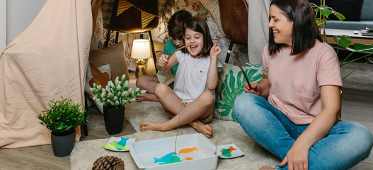 Happy mother and daughter camping at home playing diy fishing game. Home vacation concept