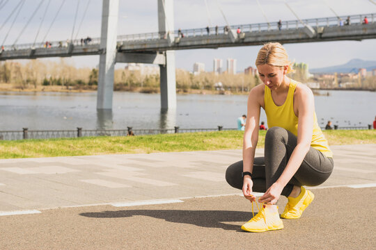 Young active woman trendy sportswear straightens her lace during sports training city street. Active healthy lifestyle