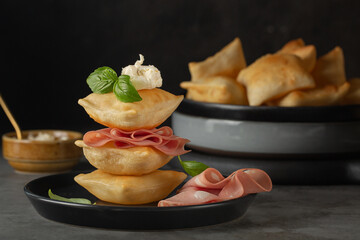Close-up of Italian fried bread crescentine or gnocco fritto with mortadella and soft cheese, decorated with basil leaves. Traditional Bologna appetizer. Dark background. - obrazy, fototapety, plakaty
