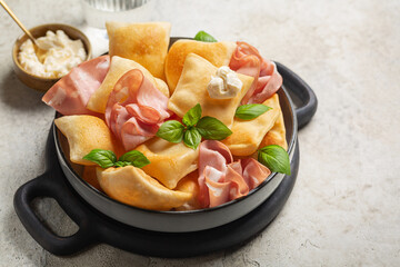 Italian aperitif with fried bread crescentine or gnocco fritto, mortadella and soft cheese, decorated with basil leaves. Traditional Bologna appetizer. Light background. - obrazy, fototapety, plakaty