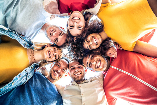 Multiracial group of young people standing in circle and smiling at camera - Happy diverse friends having fun hugging together - Low angle view - Powered by Adobe