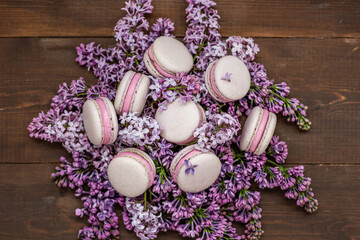 Macaroni cakes lying on a bouquet of lilacs on a dark wooden background.