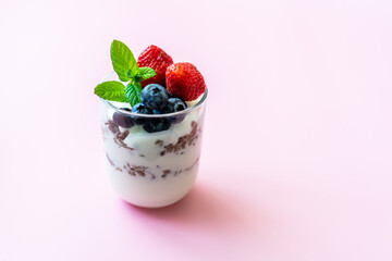 Joghurt mit Granola und frischen Beeren in einem Glas geschichtet. Gesundes Frühstück, pinker Hintergrund, Nahaufnahme.