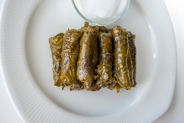Grape leaves with olive oil from the top on a white plate. 
Stuffed grape leaves with olive oil. 
Yogurt in a glass bowl.Horizontal.