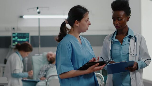 Woman nurse showing medical expertise using tablet computer to specialist black doctor woman. Hospitalized patient discussing healthcare treatment during recovery consultation