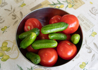 Cucumbers and tomatoes in a metal bowl on tablecloths
