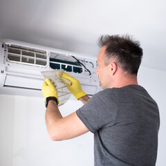 handsome man wearing yellow gloves removing air filter from air conditioner