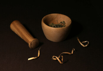 Old wooden mortar inside which green spices and pestle on a dark wooden background with wood...