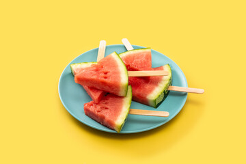 Watermelon slices popsicles on blue plate and yellow background