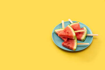 Watermelon slices popsicles on blue plate and yellow background. Copy space