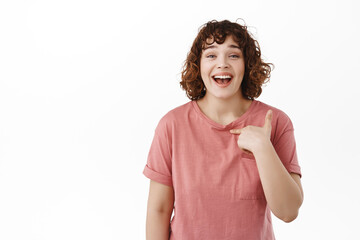 Happy beautiful woman pointing at herself, laughing and smiling with white perfect teeth, being chosen, promoted or got job, self-promoting or bragging, standing over white background