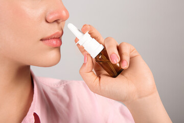 Woman using nasal spray on light grey background, closeup. Space for text - obrazy, fototapety, plakaty