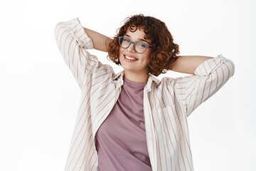 Naklejka premium Portrait of curly girl in glasses resting on day off, relaxing and smiling happy, standing carefree with happy face, looking straight at camera, white background