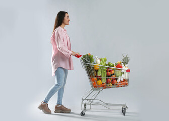 Young woman with shopping cart full of groceries on grey background © New Africa