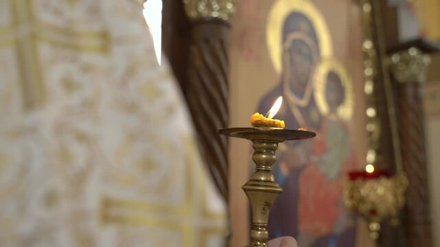 Candle in the hands of a priest on a background with a blurry image of the Mother of God