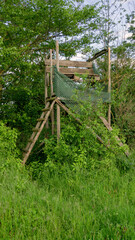 Lookout wooden ladder seat, also known as hunter's seat, hunter's high seat between the trees in nature for observing wild animals, animal world covered with camouflage hunting camouflage net