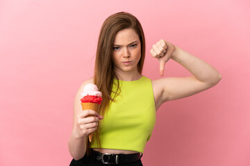 Teenager girl with a cornet ice cream over isolated pink background showing thumb down with negative expression