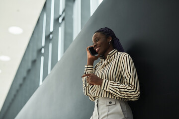 Graphic side view portrait of smiling African-American businesswoman speaking by smartphone while standing against black background