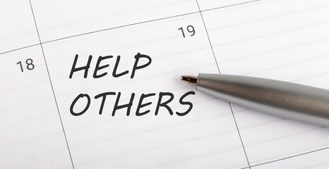 Text HELP OTHERS on calendar planner to remind you an important appointment with pen on isolated white background.