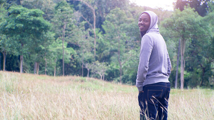African man is wearing hooded shirt and standing on the field in beutiful meadow.Happy and enjoy nature concept