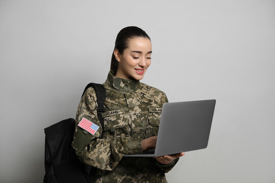 Female soldier with laptop and backpack on light grey background. Military education