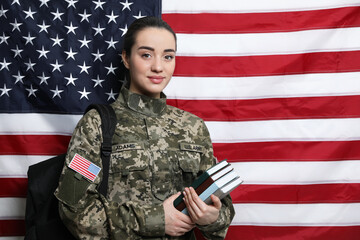 Female soldier with backpack and books near flag of United States, space for text. Military...