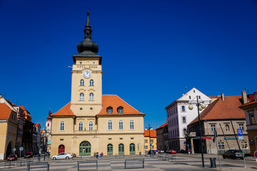 Yellow classic town hall with clock tower at main Freedom square, renaissance and baroque historical buildings, blue sky, Medieval street, sunny day, Zatec, Bohemia, Czech Republic