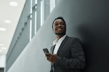 Graphic low angle portrait of carefree African-American businessman holding smartphone while...