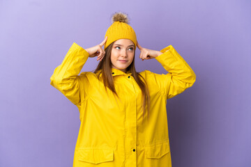 Teenager girl wearing a rainproof coat over isolated purple background having doubts and thinking