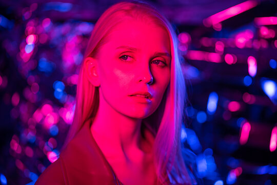 Portrait of a stylish model in colored lights. Young blond woman on a shimmering background.